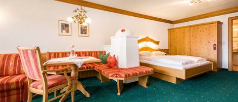 A hotel room with a wooden bed, a bench, a dining table with chairs, and a sofa.