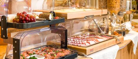 Un bufé con diversos alimentos, incluyendo carnes y frutas, exhibidos en recipientes transparentes.