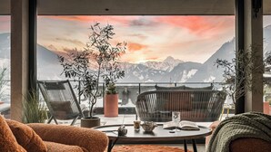 A modern living room with a large window overlooking mountains, featuring a round table, two chairs, and a potted plant. - Hotel Sieghard (Schwendau)