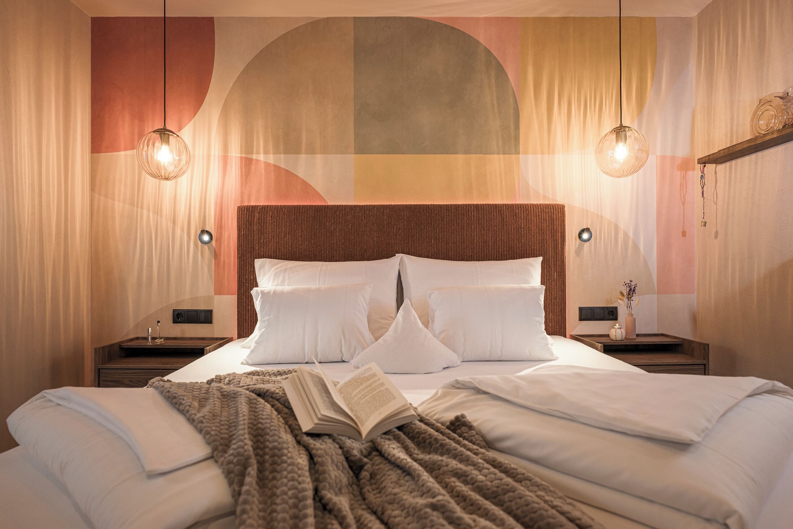 A hotel room with a large bed, two bedside tables, a wall-mounted light fixture, and a decorative wall panel.