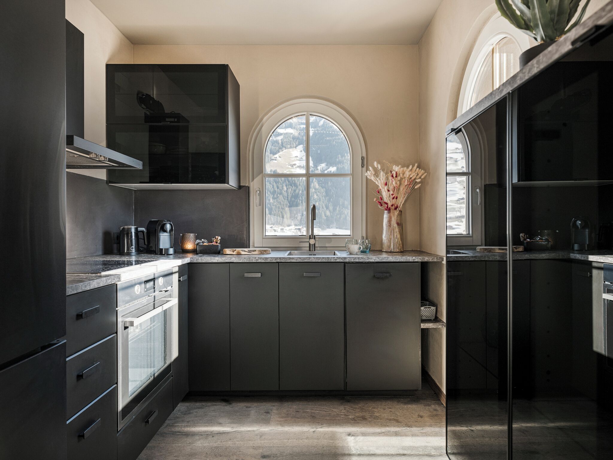 Una cocina moderna con armarios oscuros, un ventanal y vistas a un paisaje nevado.
