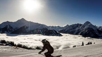 A skier on a snowy slope with a mountain range in the background and the sun shining.