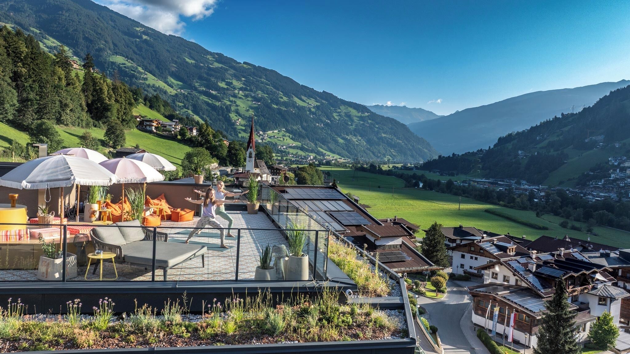A rooftop terrace with a glass balustrade, outdoor seating, and a view of a mountainous landscape.