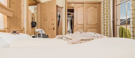 A bedroom with a large bed, wooden wardrobe, and a closet with hanging clothes.