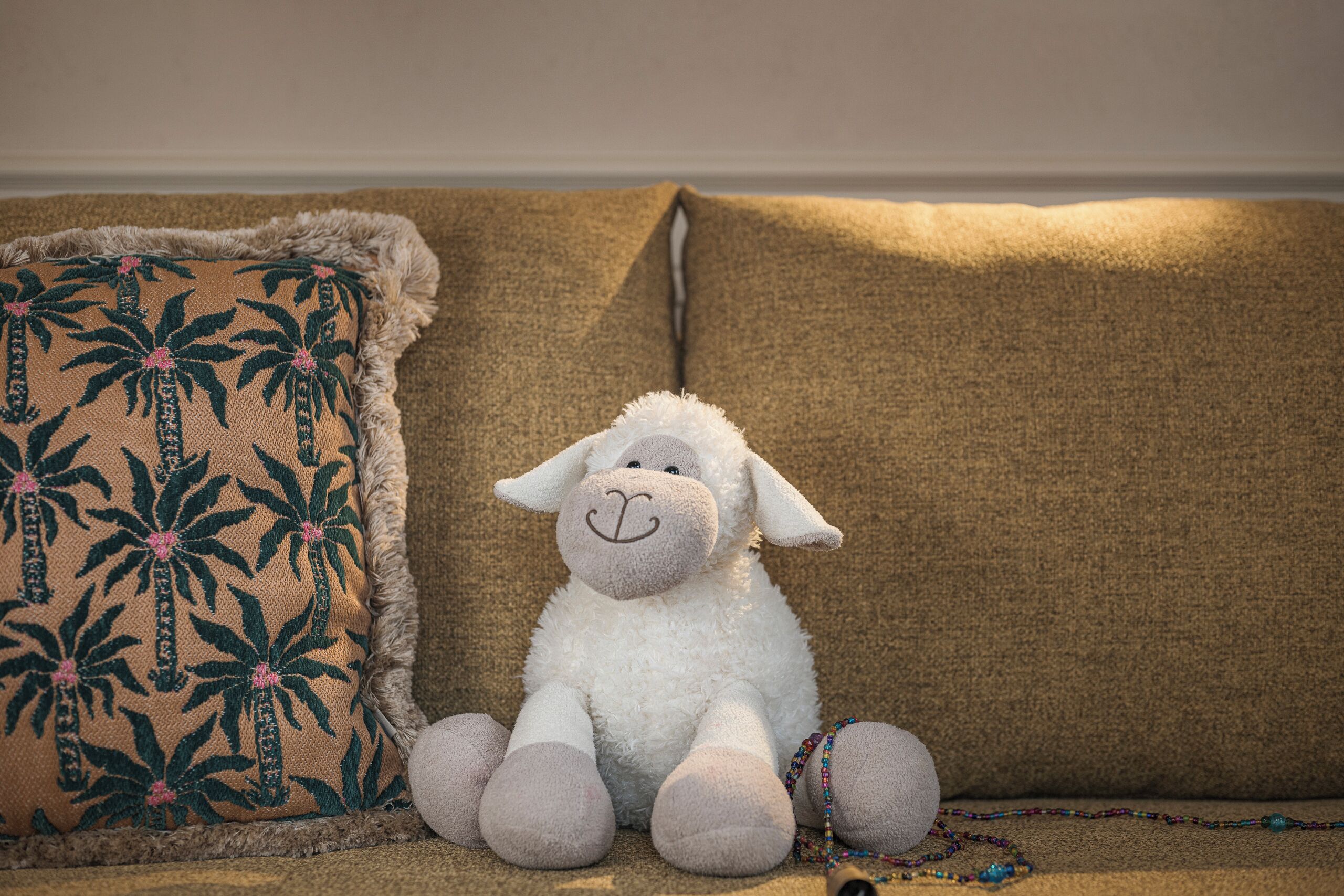 Un borrego de peluche sobre un sofá con un cojín estampado.