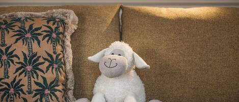 Un borrego de peluche sobre un sofá con un cojín estampado.