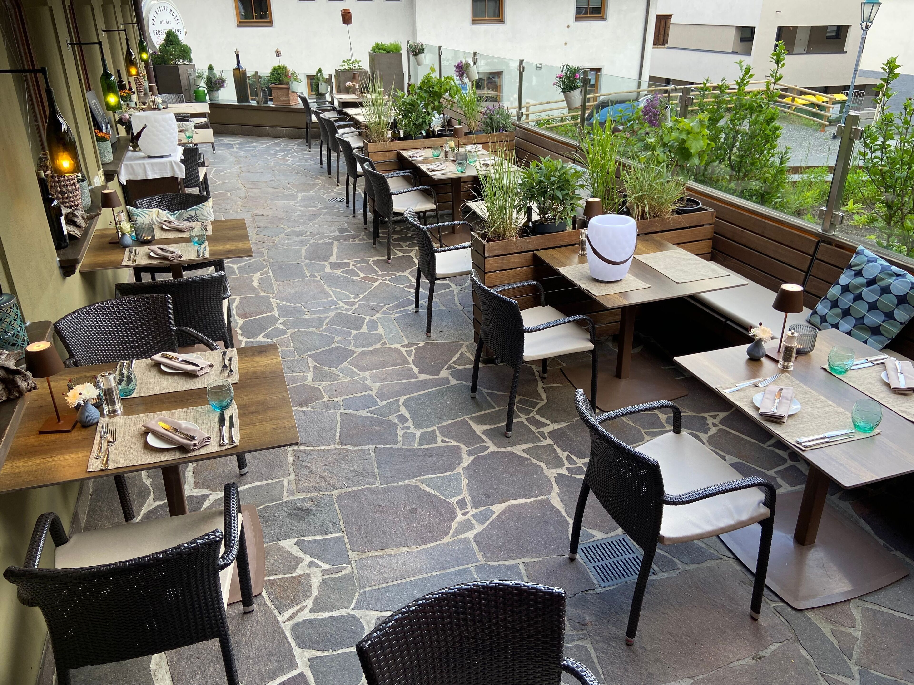 An outdoor seating area with stone flooring, wooden tables, and black wicker chairs.