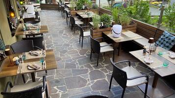 An outdoor seating area with stone flooring, wooden tables, and black wicker chairs.