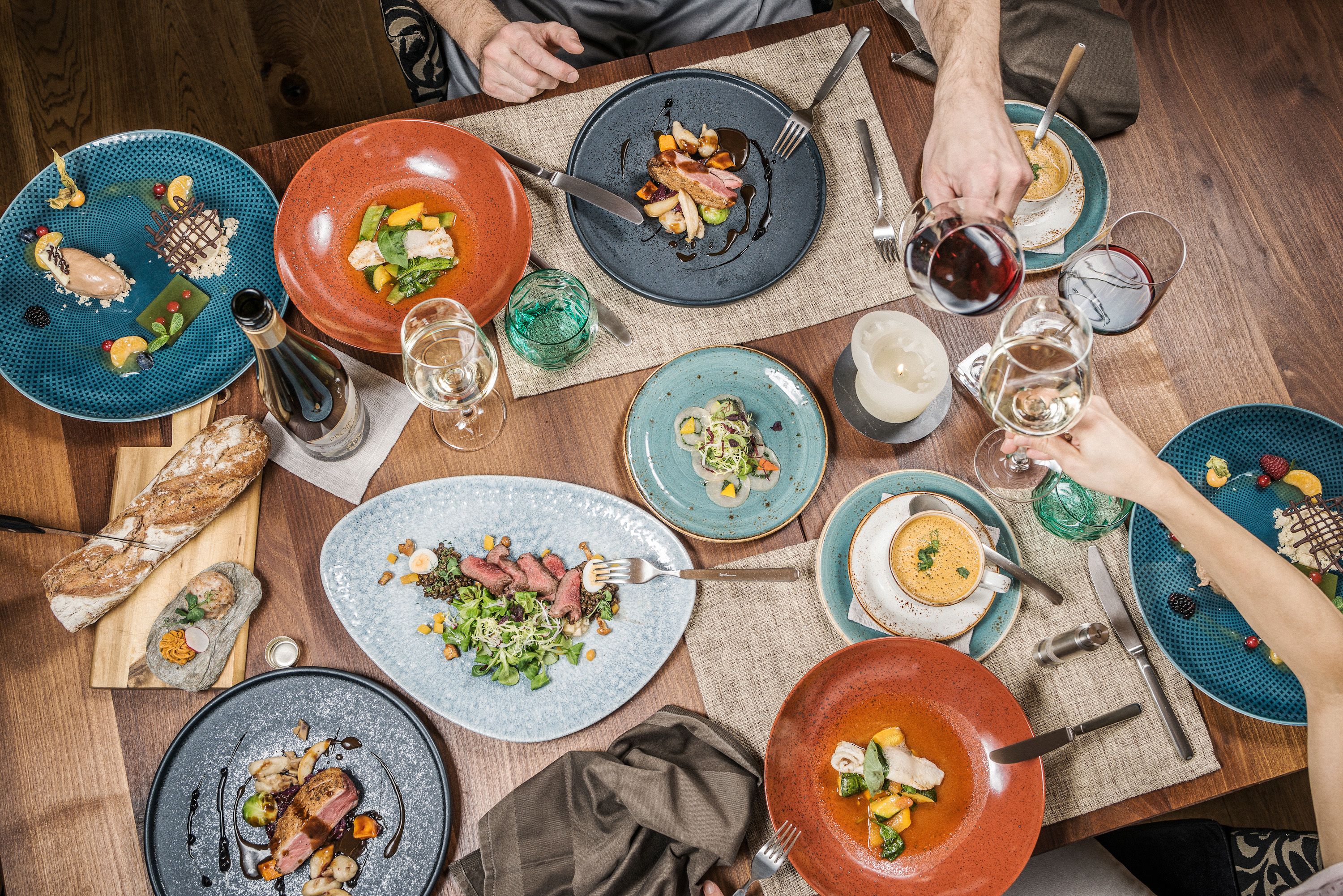 Una mesa de comedor puesta con diversos platos, entre ellos un bistec, sopa y ensalada, además de varias copas de vino y cubiertos.