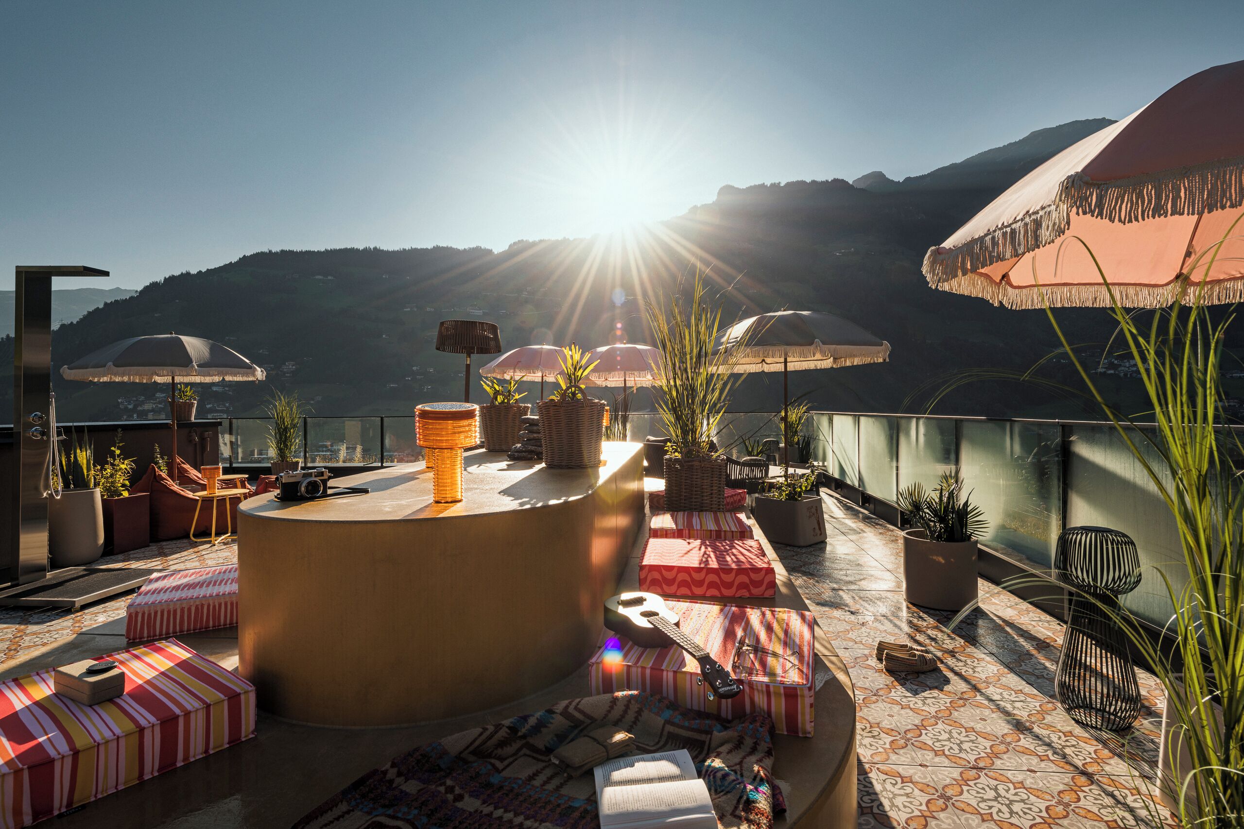 A rooftop terrace with a panoramic mountain view, outdoor seating, and a variety of plants.