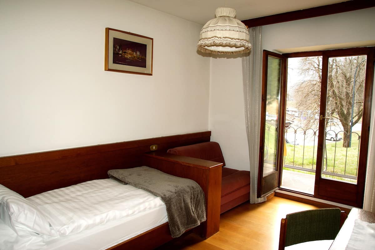 A bedroom with a bed, a chair, a sofa, a window with a view of the outside, and a hanging light fixture.