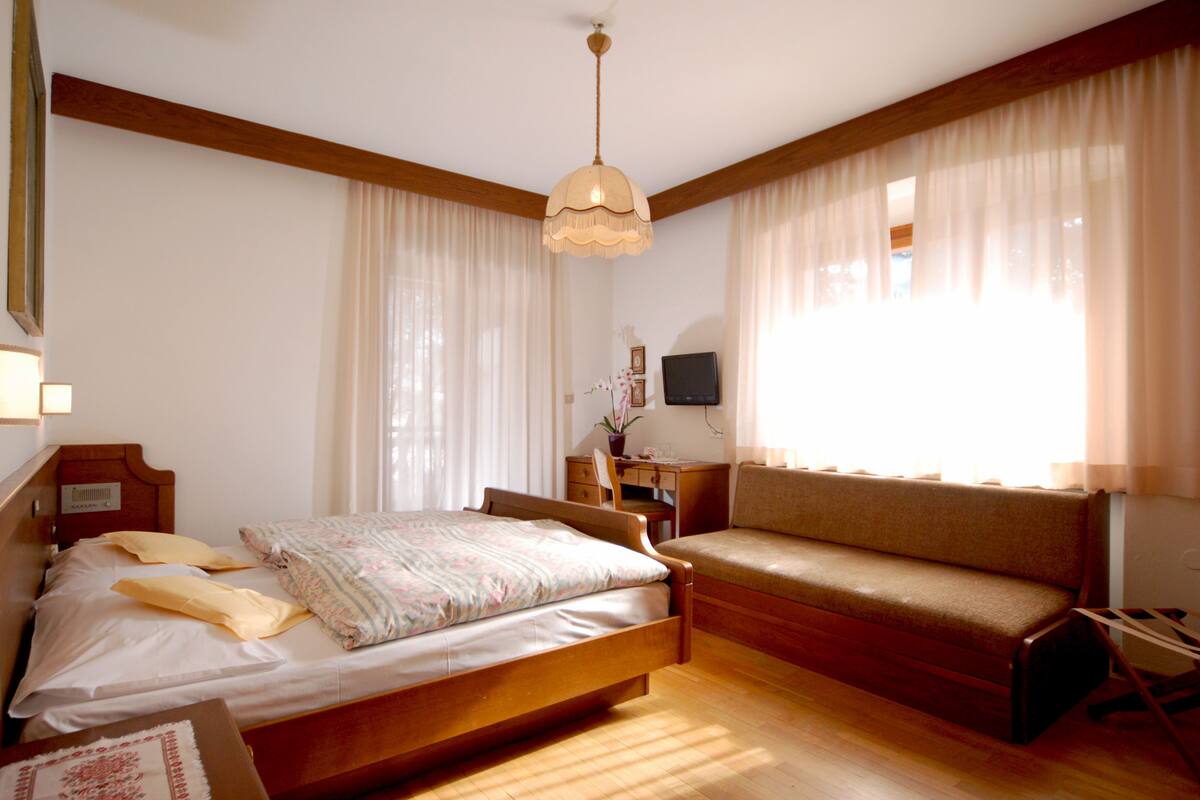 A bedroom with a wooden bed, a wooden bench, a desk, and a chair.
