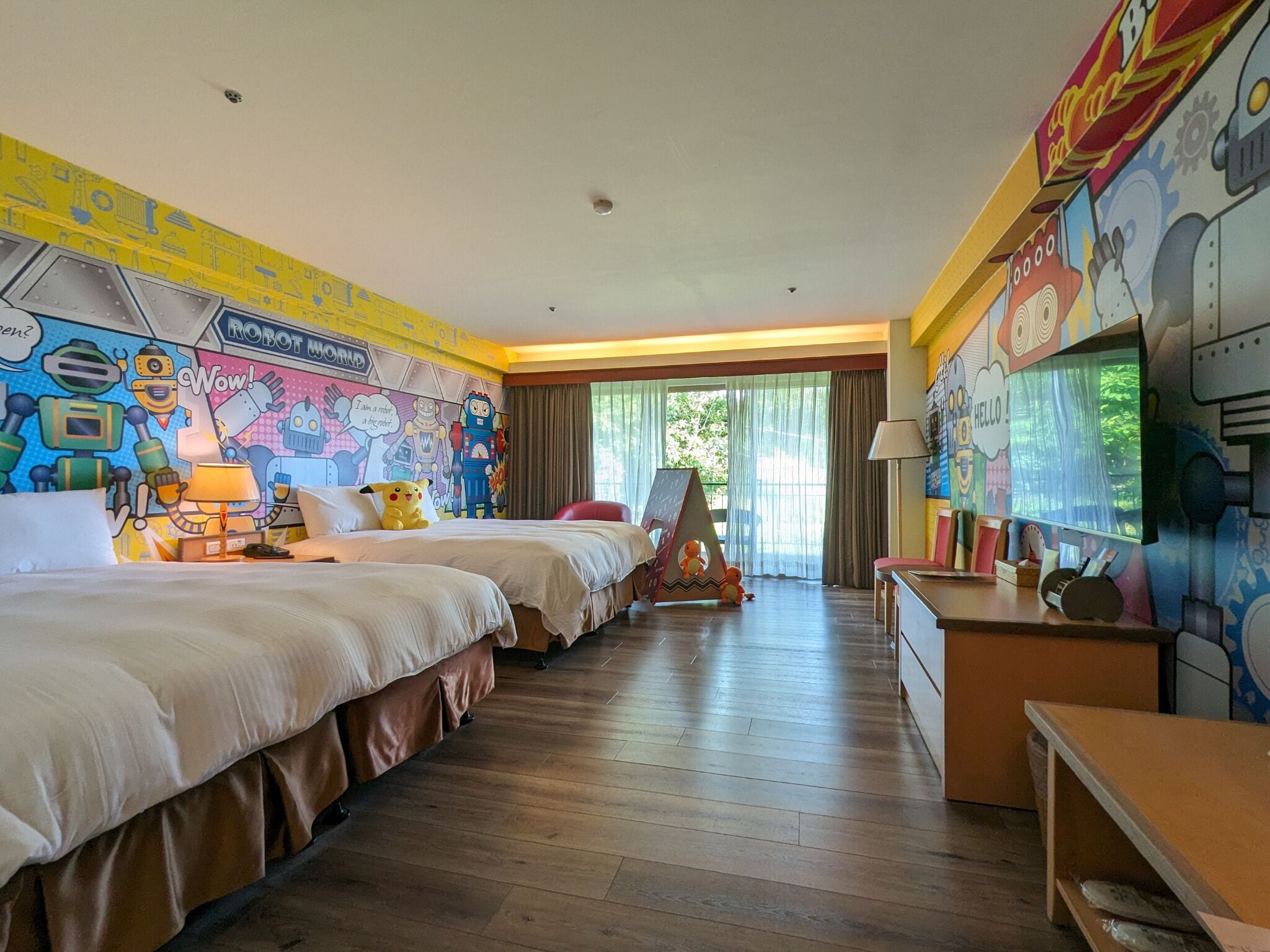 Una camera d'albergo con due letti, una scrivania e un murale alle pareti.