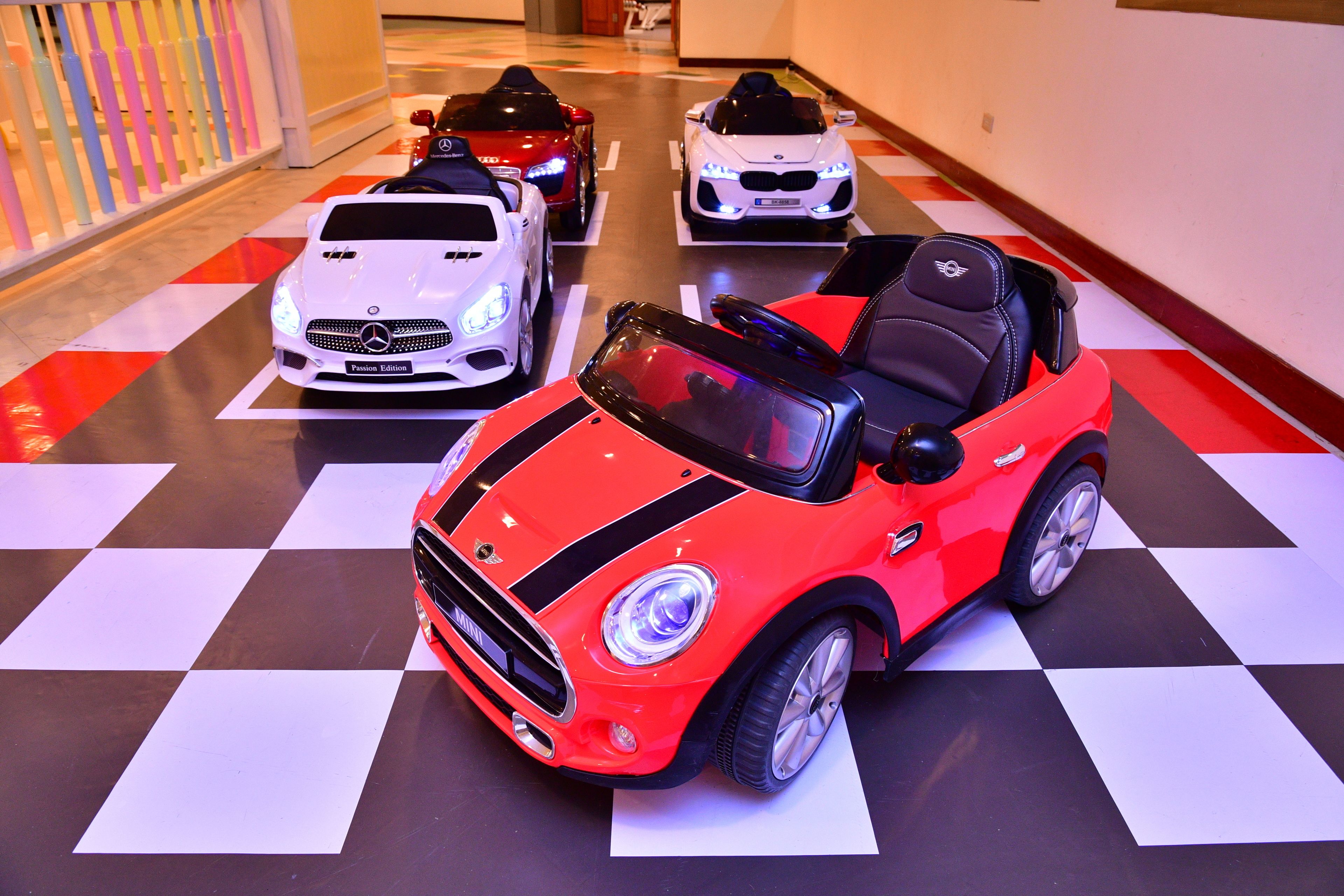 A red Mini Cooper toy car on a checkered floor with other toy cars.