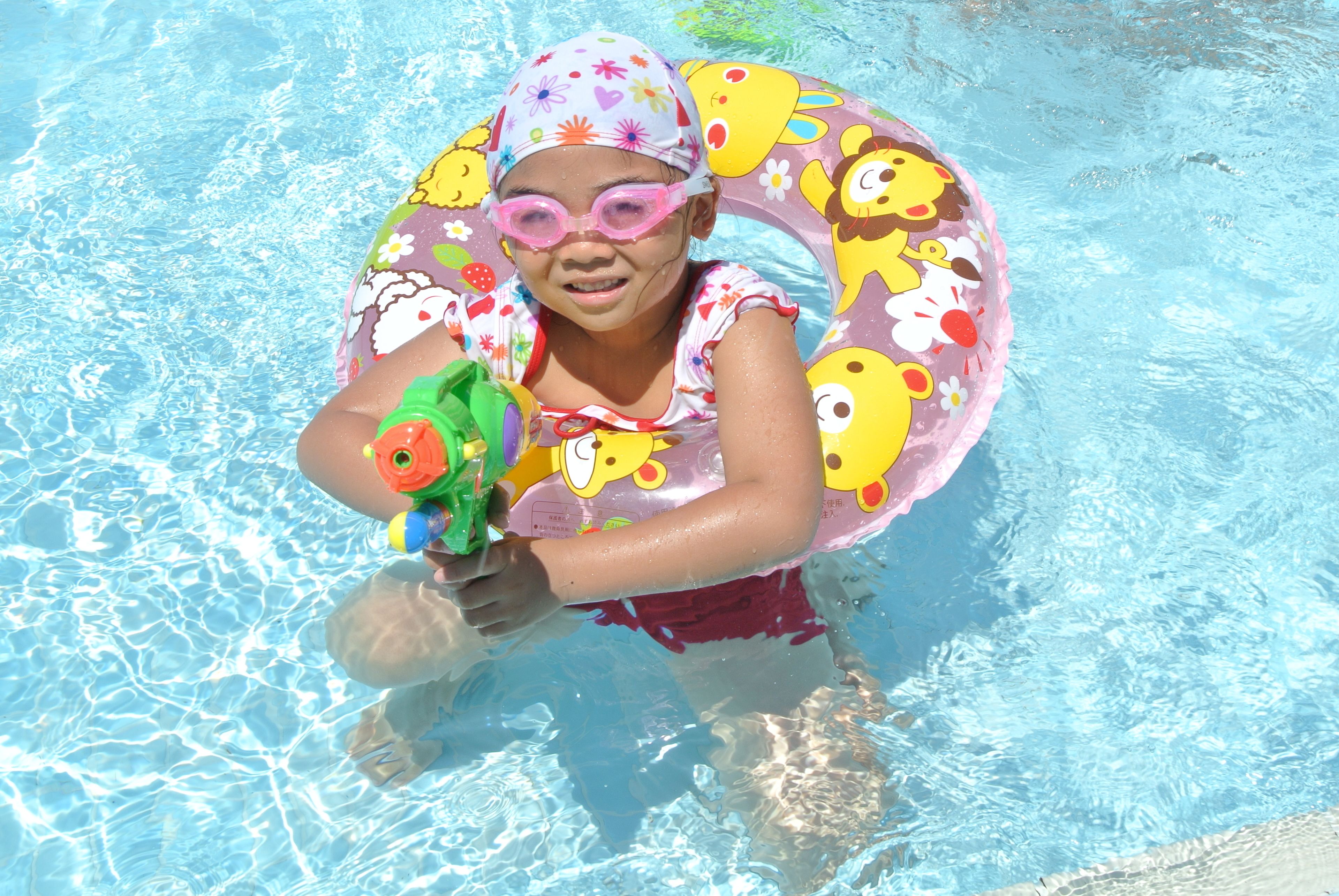 A child in a swimming pool with a colorful inflatable ring and a water gun.