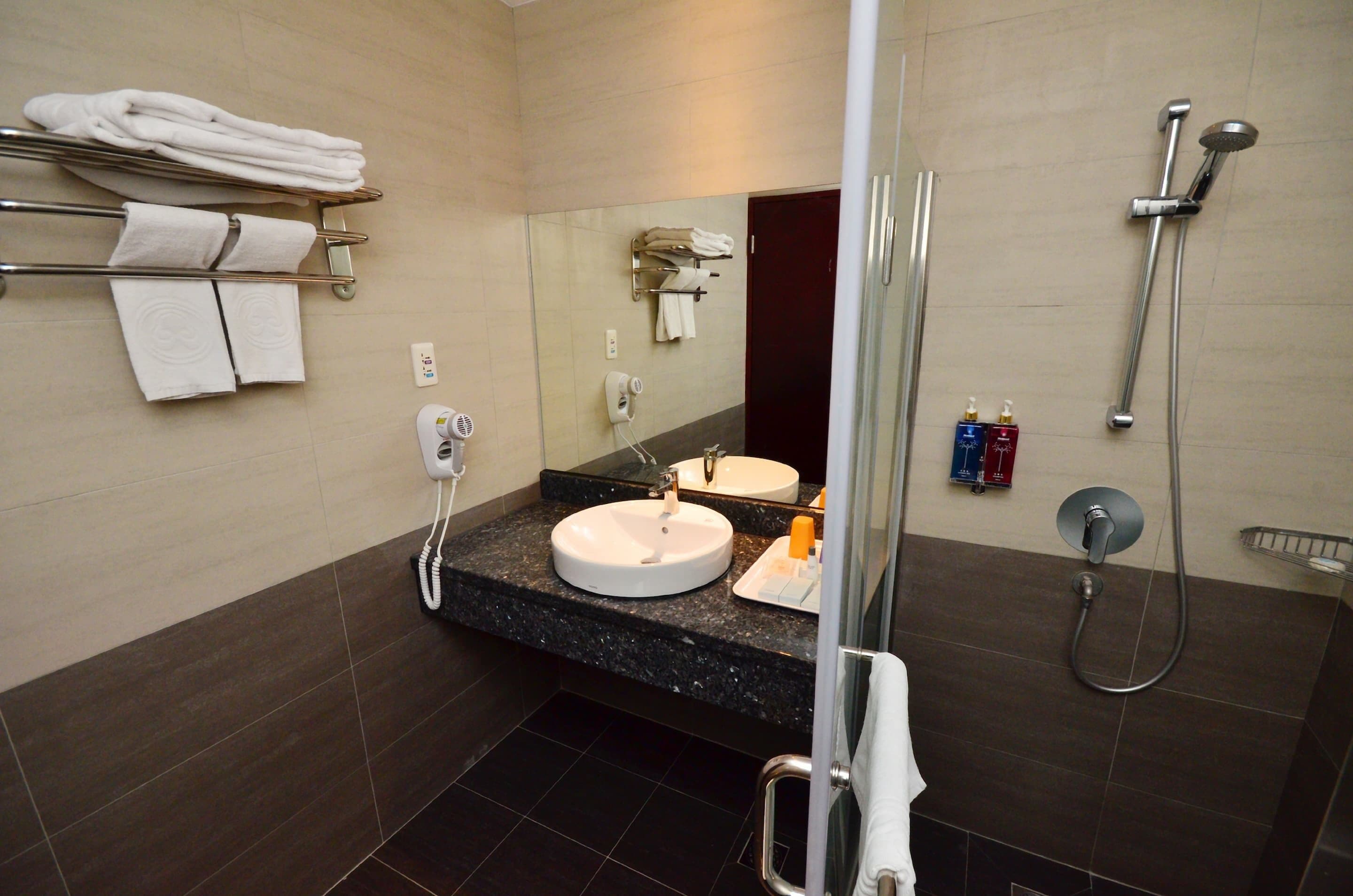 Un baño con lavamanos, espejo, toallero, ducha y artículos de tocador.