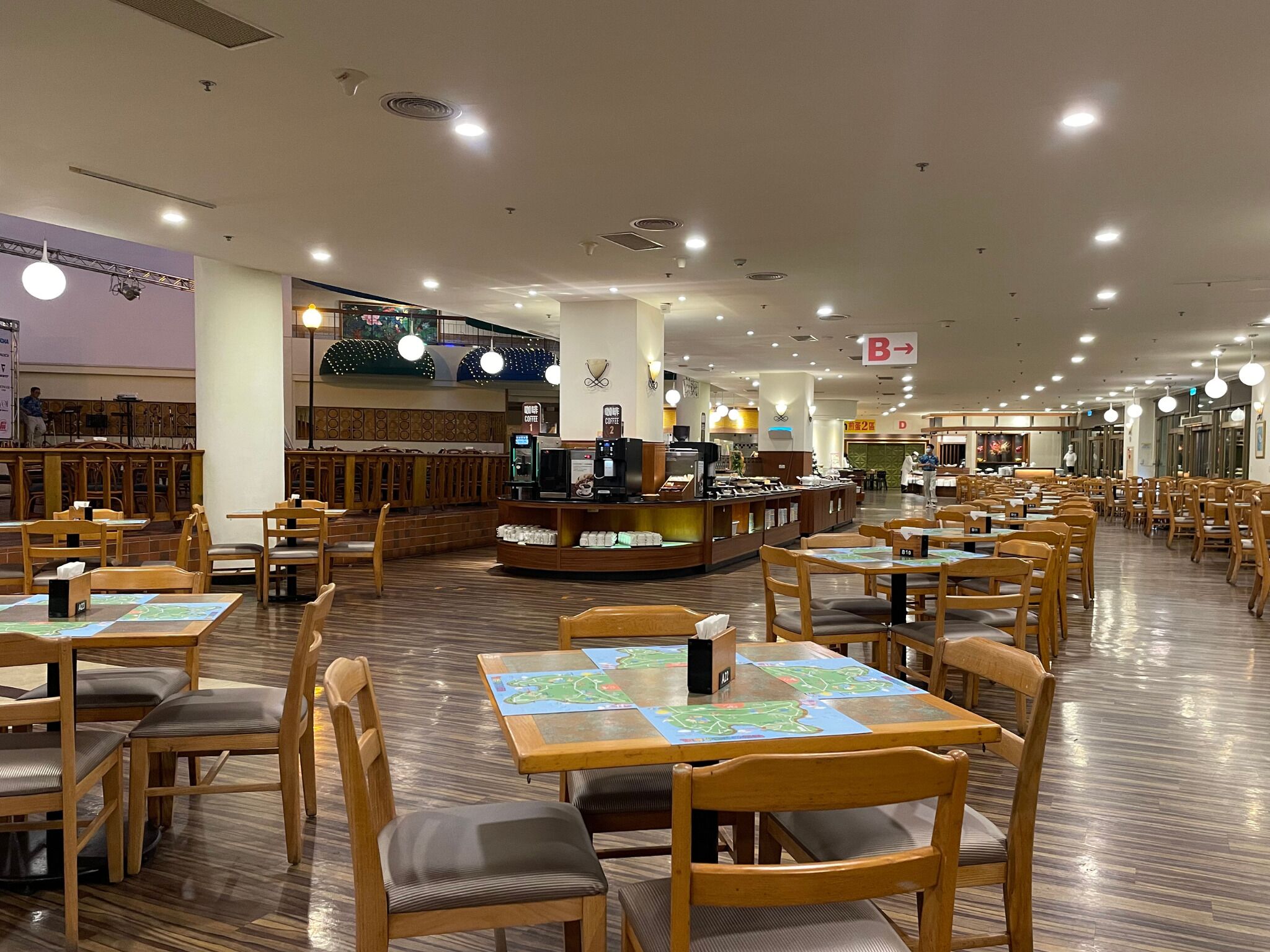 A spacious restaurant with wooden tables and chairs, a coffee bar, and a stage area.