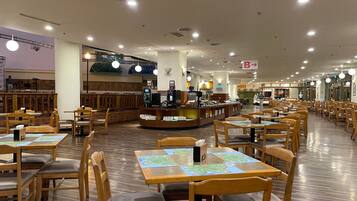 A spacious restaurant with wooden tables and chairs, a coffee bar, and a stage area.
