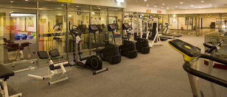 A gym with various exercise machines, including treadmills and weight stations, arranged in rows.