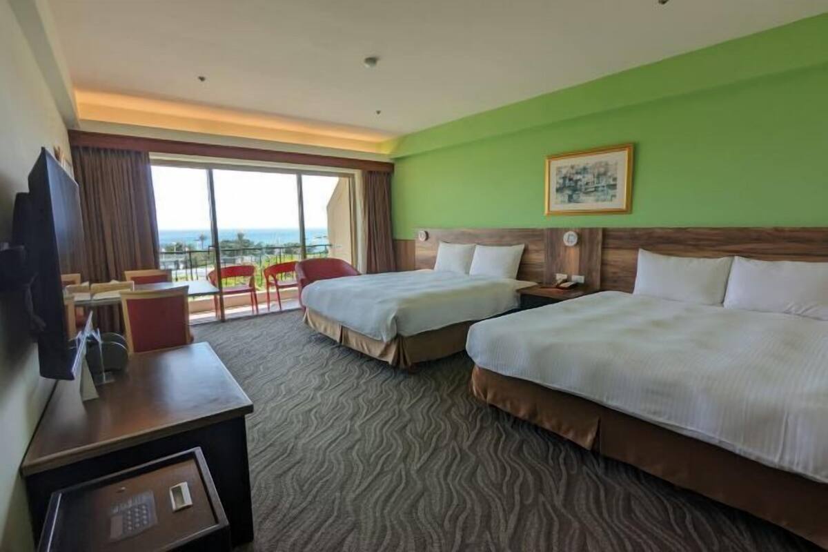 A hotel room with two beds, a desk, a chair, a television, and a large window with a view.