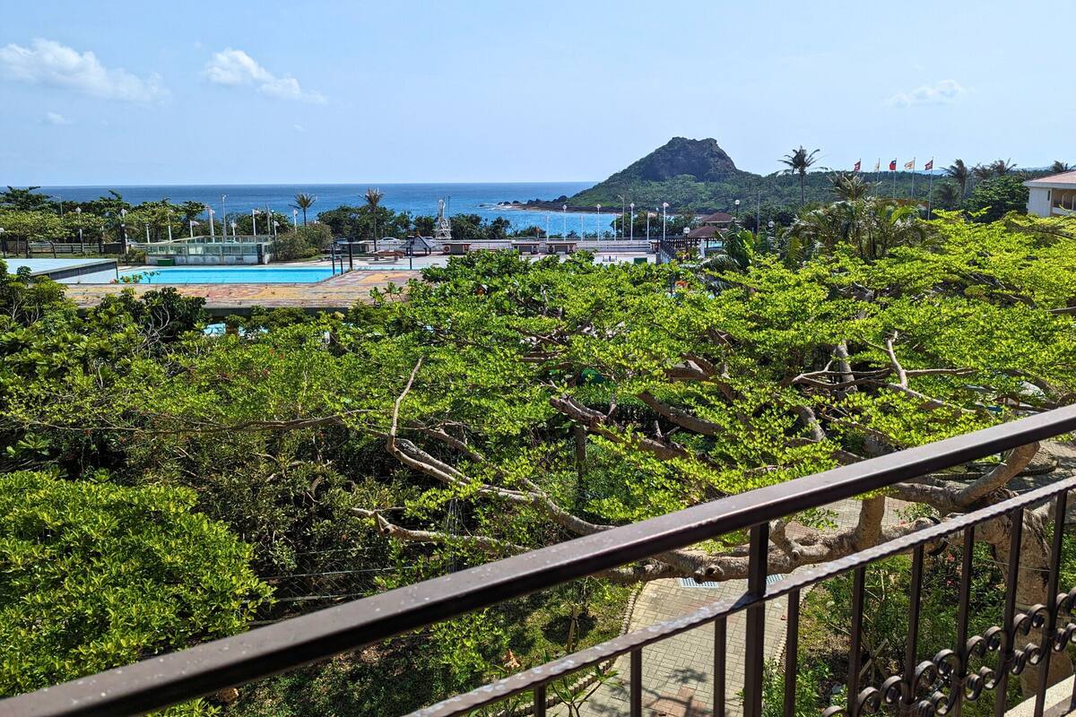 A view of a lush green landscape with a pool area and a distant mountain.