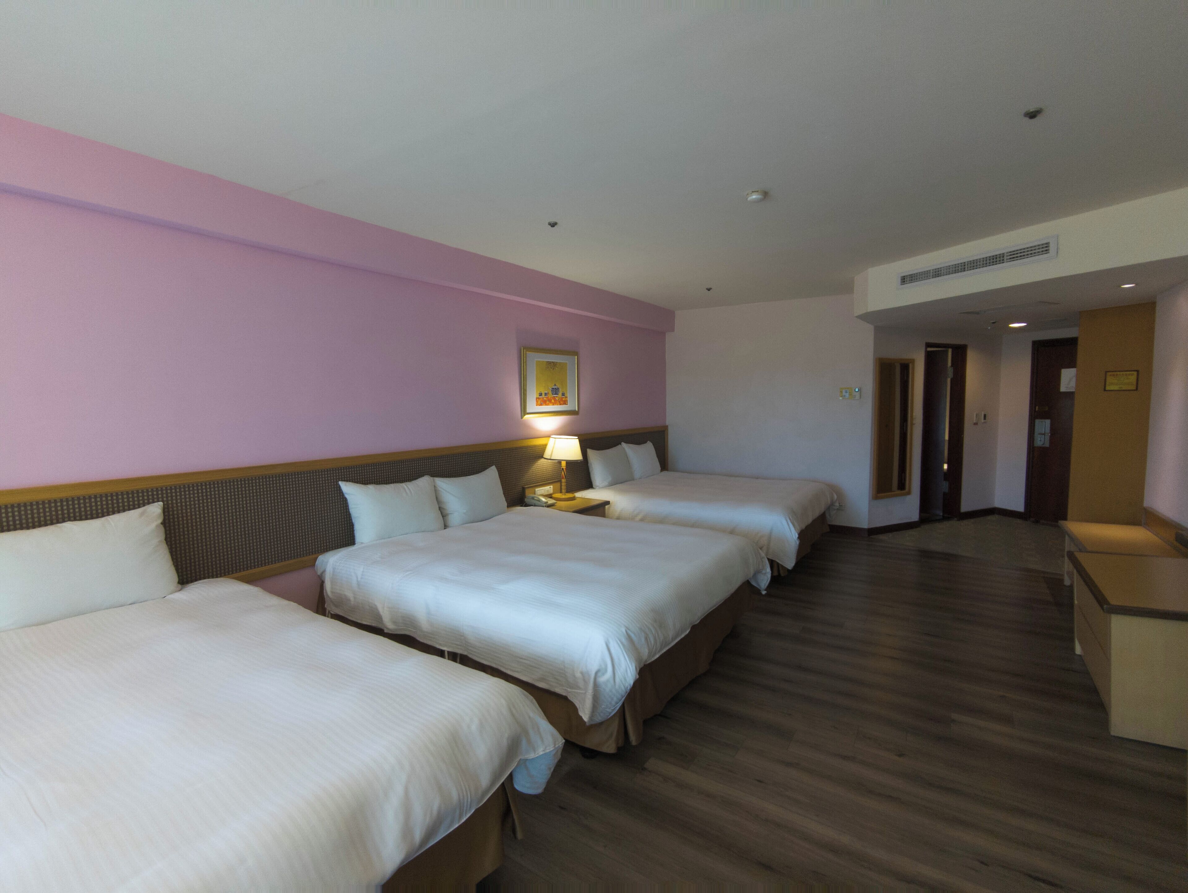 Een hotelkamer met twee bedden, een nachtkastje met een lamp en een houten vloer.