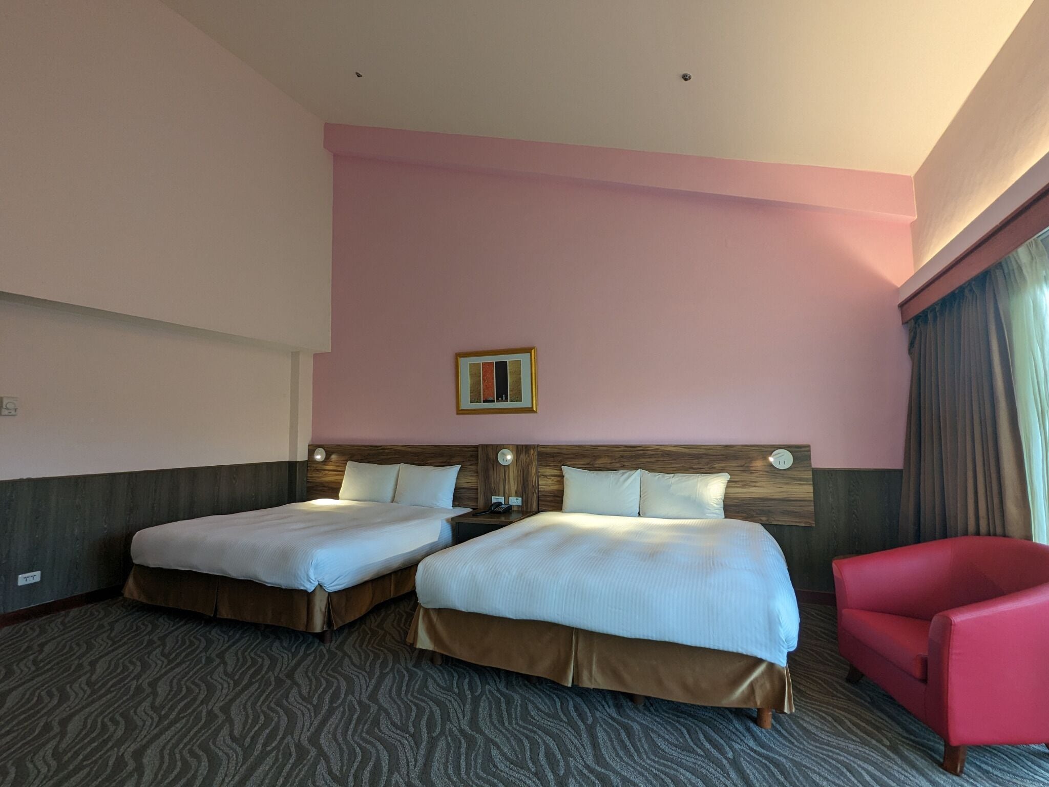 Habitación de hotel con dos camas, un sillón rojo y un cuadro en la pared.