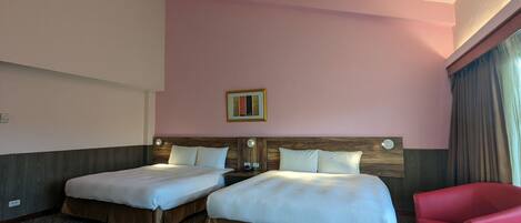 A hotel room with two beds, a red armchair, and a painting on the wall.