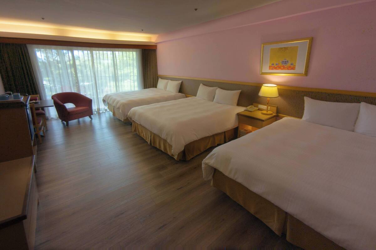 A hotel room with two beds, a desk, a chair, and a window with curtains.