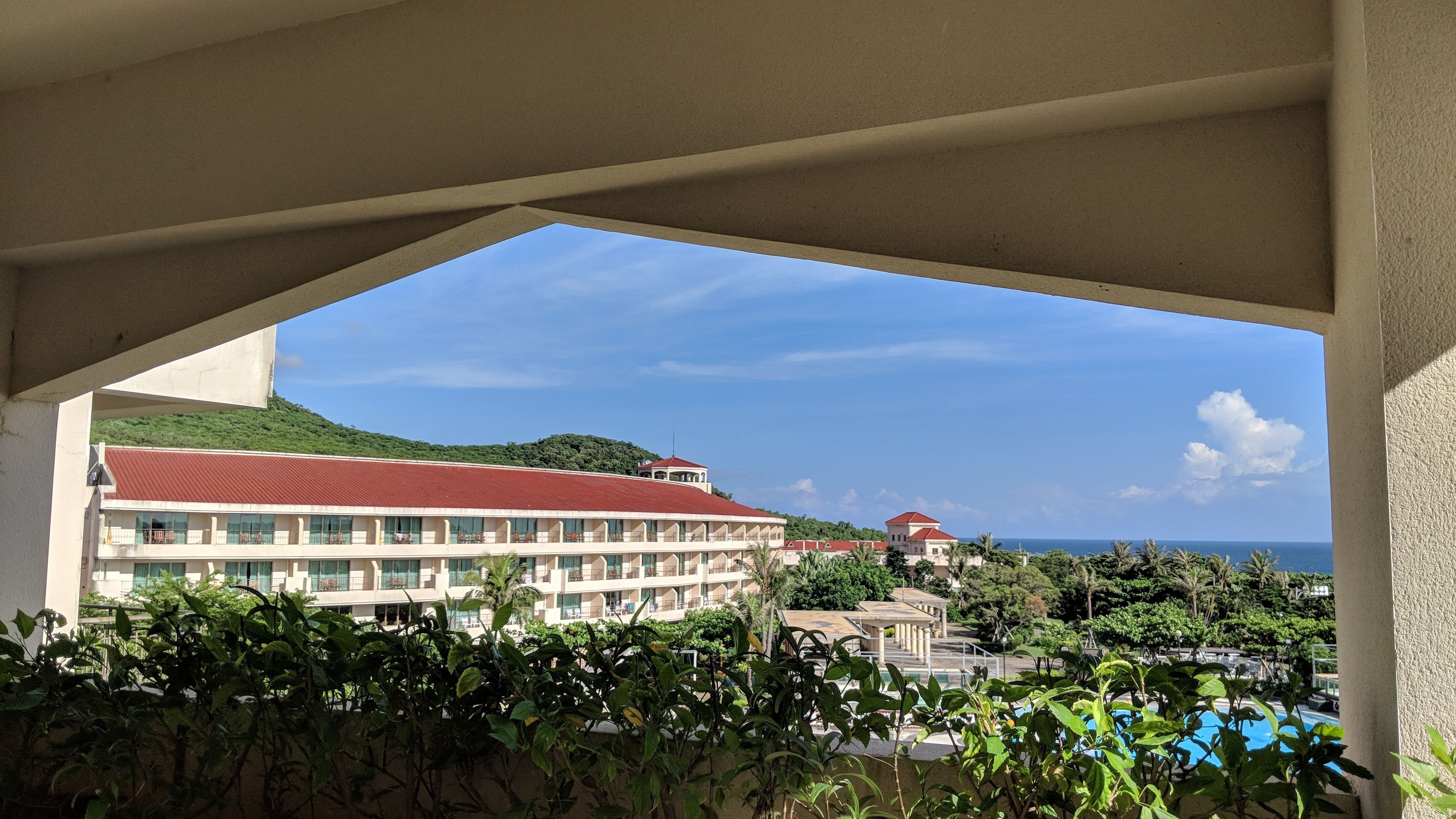 A hotel with a red-roofed building, a pool, and a view of the ocean.