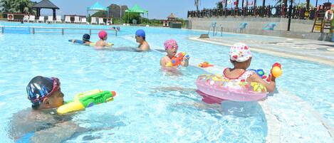 Una piscina con varias personas nadando, algunas usando dispositivos de flotación.