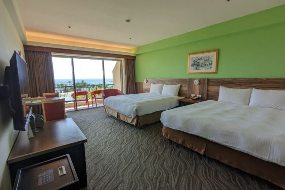 A hotel room with two beds, a desk, a chair, a television, and a large window with a view.