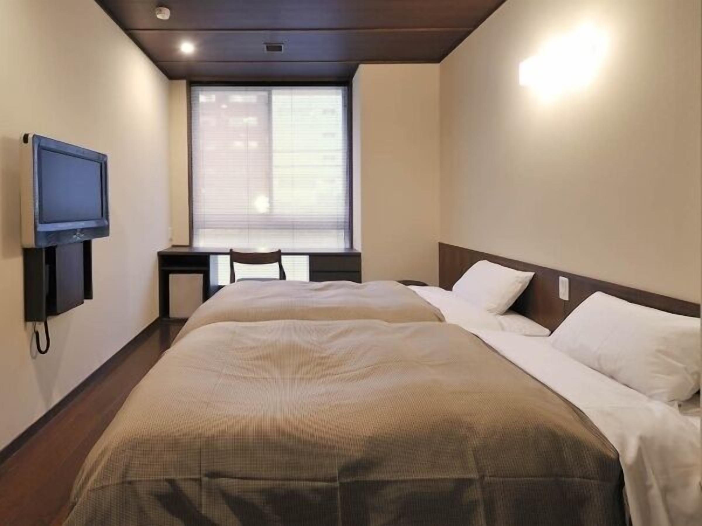 A hotel room with a bed, a television, a desk, and a window.
