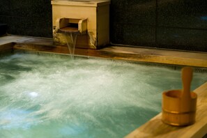 Una bañera de madera con agua corriente, un balde de madera y una pared de piedra.