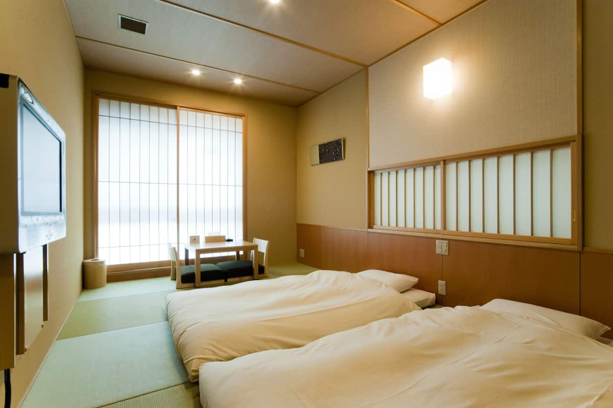 Una camera d'albergo con due letti, un futon, una scrivania con una sedia e un'ampia finestra con paraventi shoji.