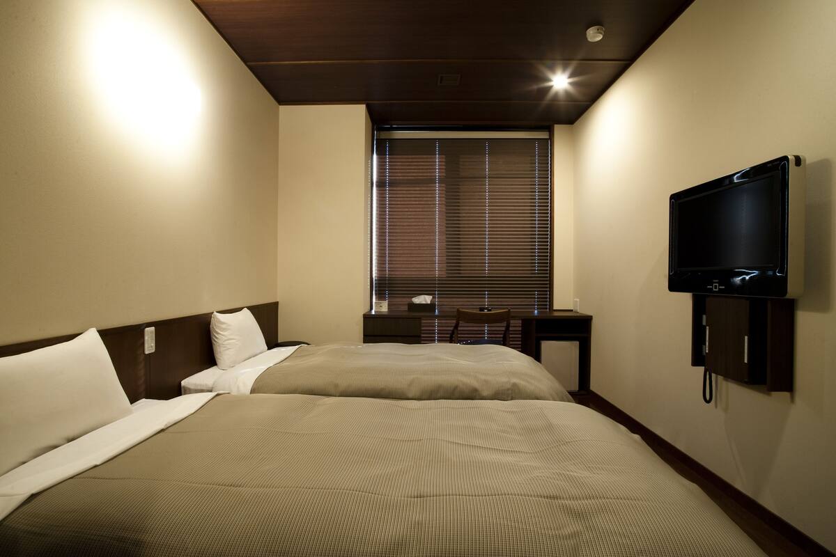 Camera d'albergo con due letti, una scrivania, una televisione e una finestra con persiane.