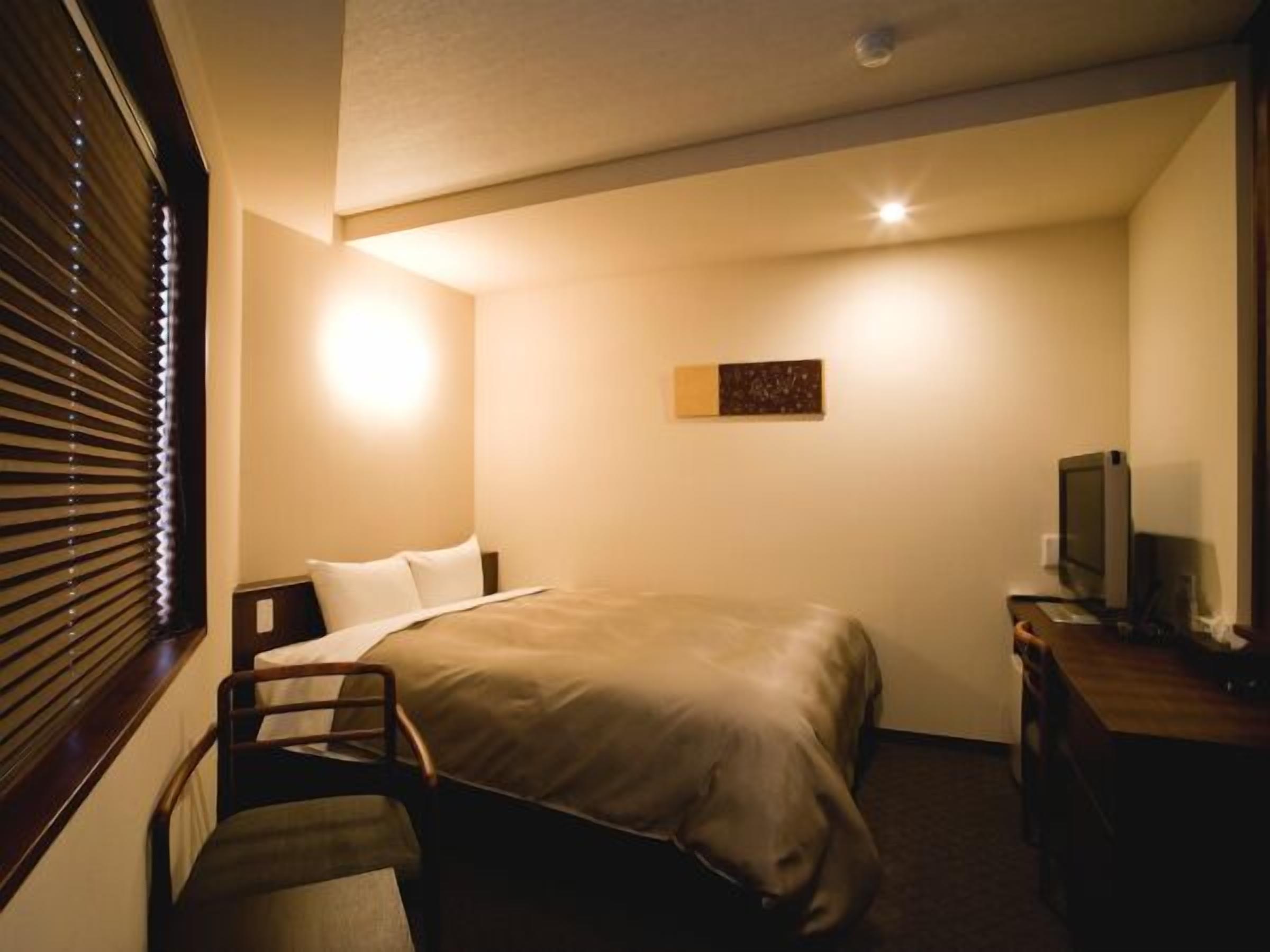 A hotel room with a bed, a desk, a chair, a television, and a window with blinds.