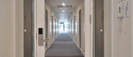 A hotel corridor with doors numbered 2101-2118, a phone on the wall, and an emergency exit sign.