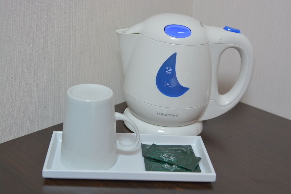 A white electric kettle with a blue digital display, a white mug, and a small tray with green packets.