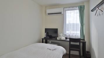 A hotel room with a bed, a desk with a computer, a chair, an air conditioner, and a window with curtains.