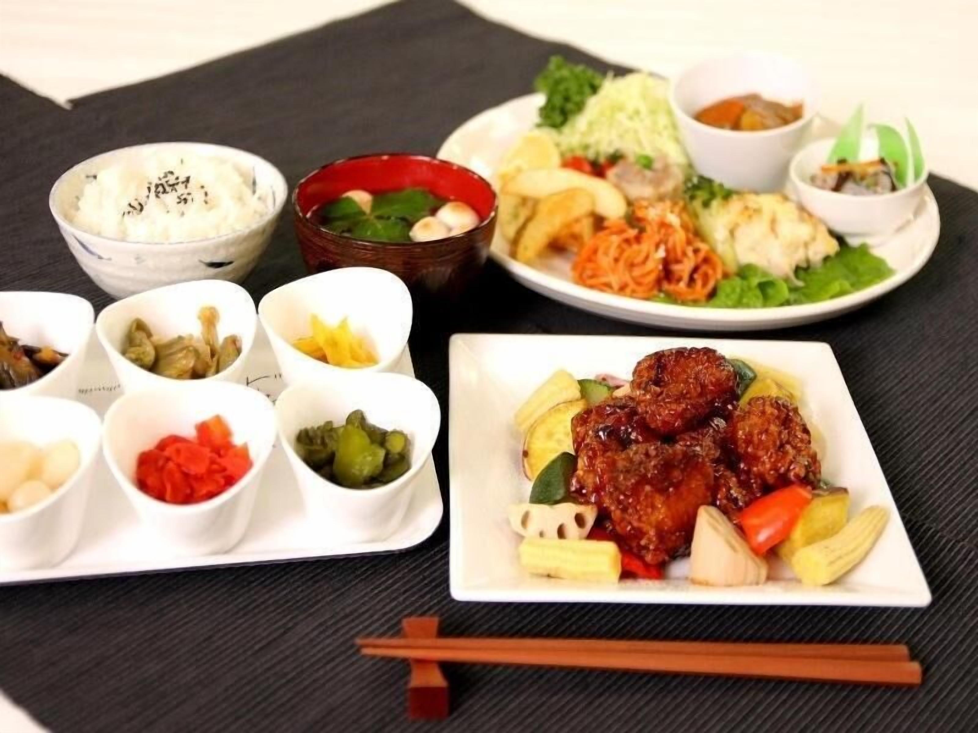 A variety of dishes including rice, vegetables, and meat, served on a table with chopsticks and bowls.