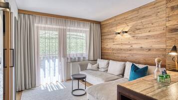 A modern living room with a wooden wall panel, a sofa, a round table, and a large window with curtains.