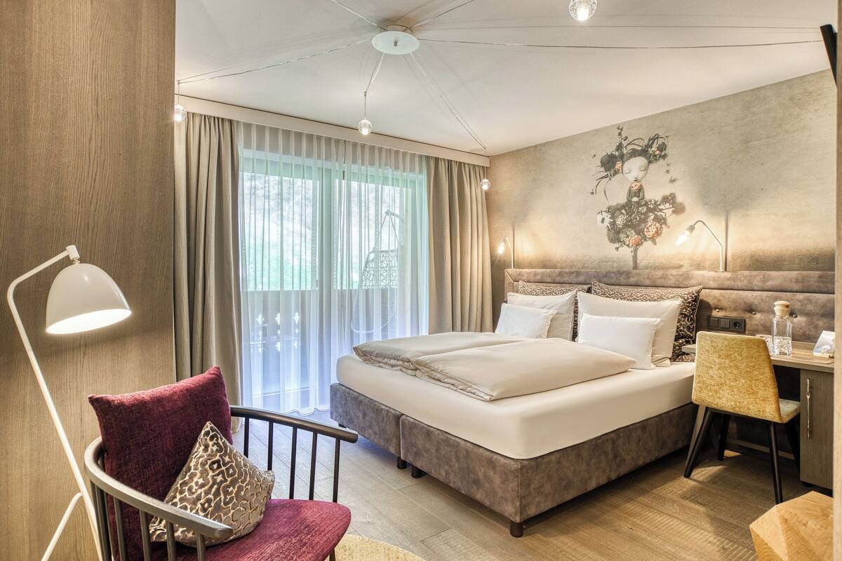 Ein Hotelzimmer mit Bett, Schreibtisch, Stuhl und einem großen Fenster mit Vorhängen.