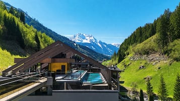 A modern building with a pool, surrounded by mountains and greenery.