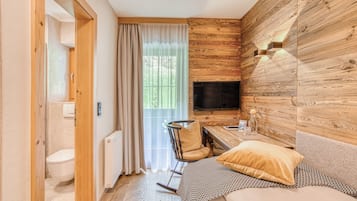 A compact room with a wooden wall, a television, a rocking chair, a sofa, and a window with curtains.