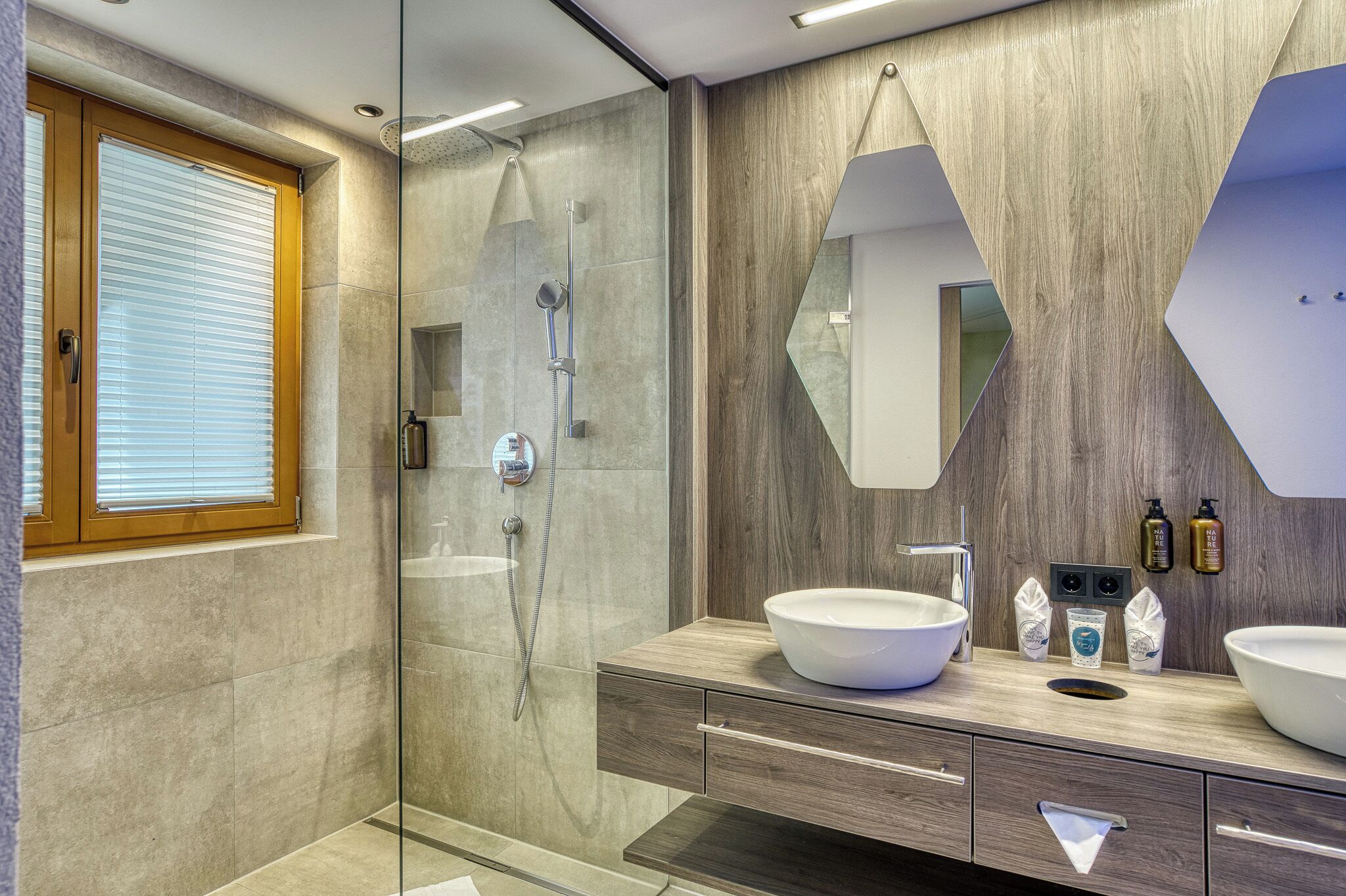 Een moderne badkamer met een douche met glazen wand, een grote spiegel en twee wastafels.