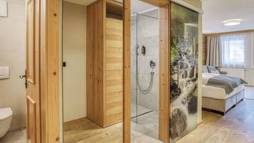 Un dormitorio moderno con ducha de vidrio, armario de madera y cama con vistas al exterior.