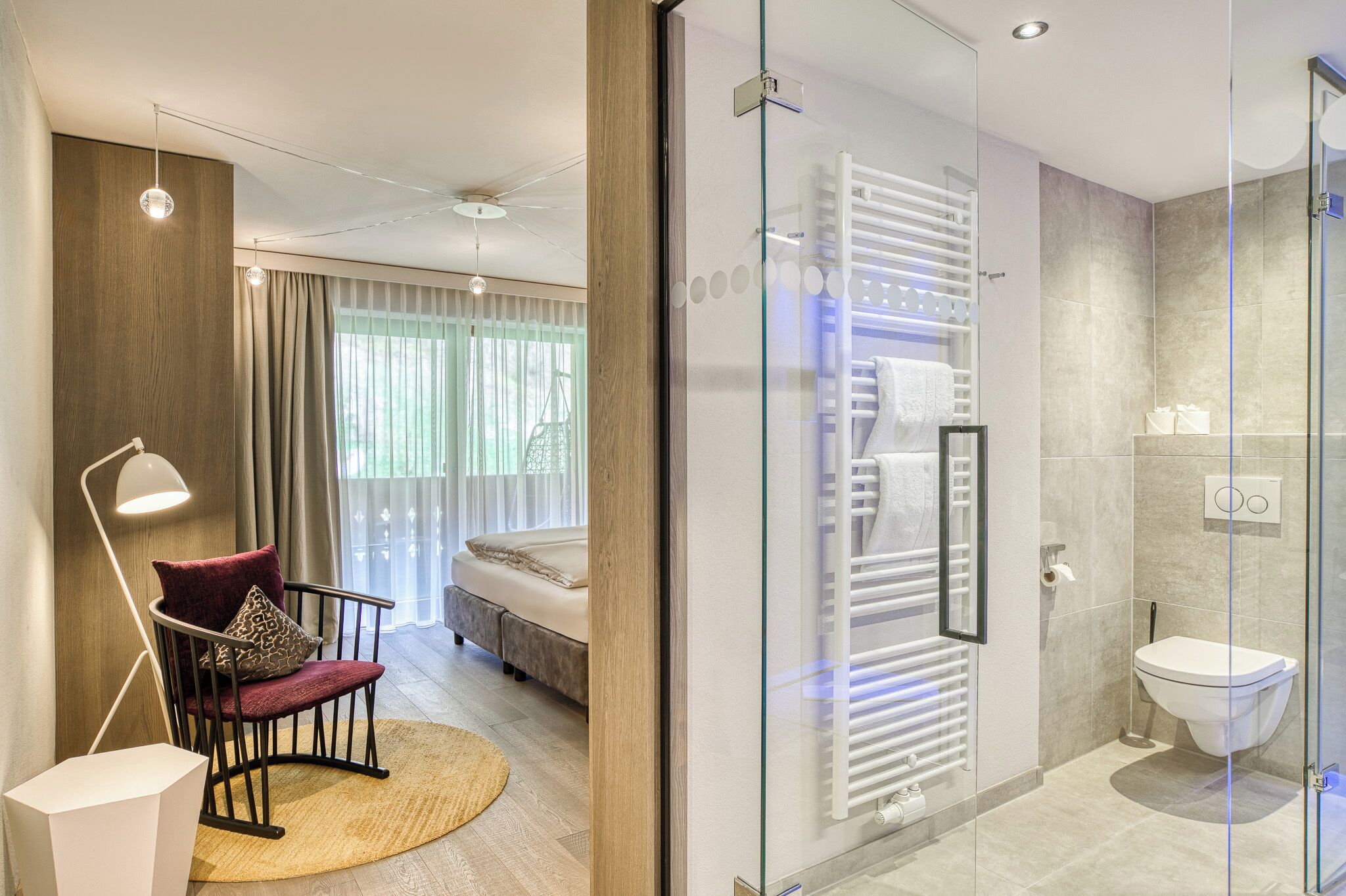 A modern hotel room with a bed, a chair, a glass shower enclosure, and a visible bathroom.