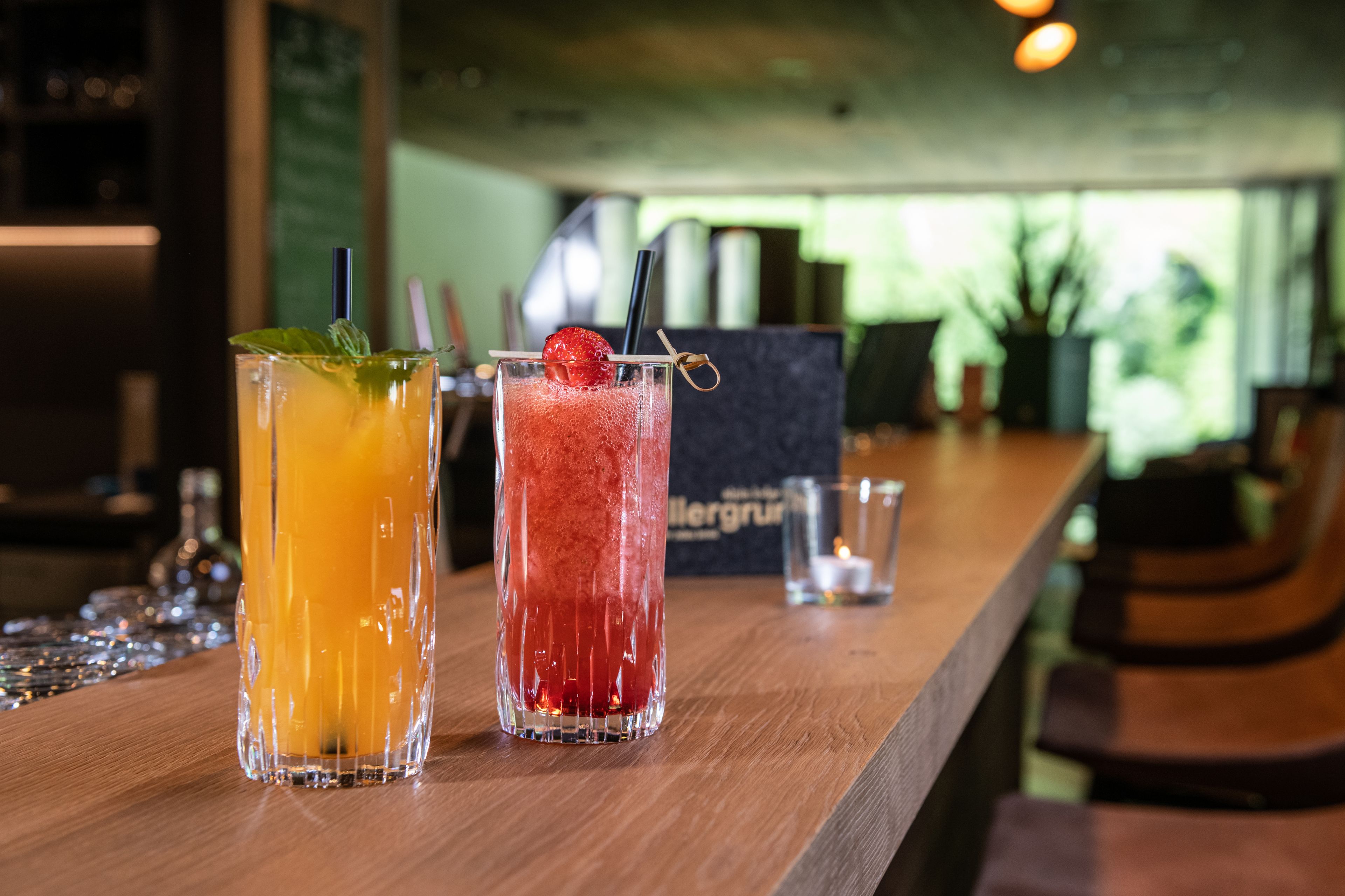 Two glasses of beverages on a wooden bar counter with a blurred background.