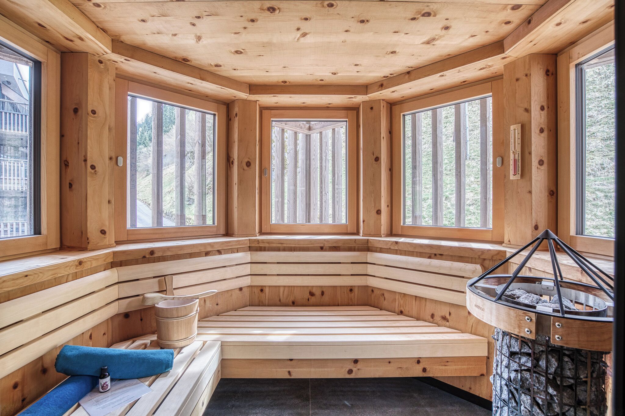 Una sauna de madera con bancos, ventanas amplias y una chimenea de piedra.